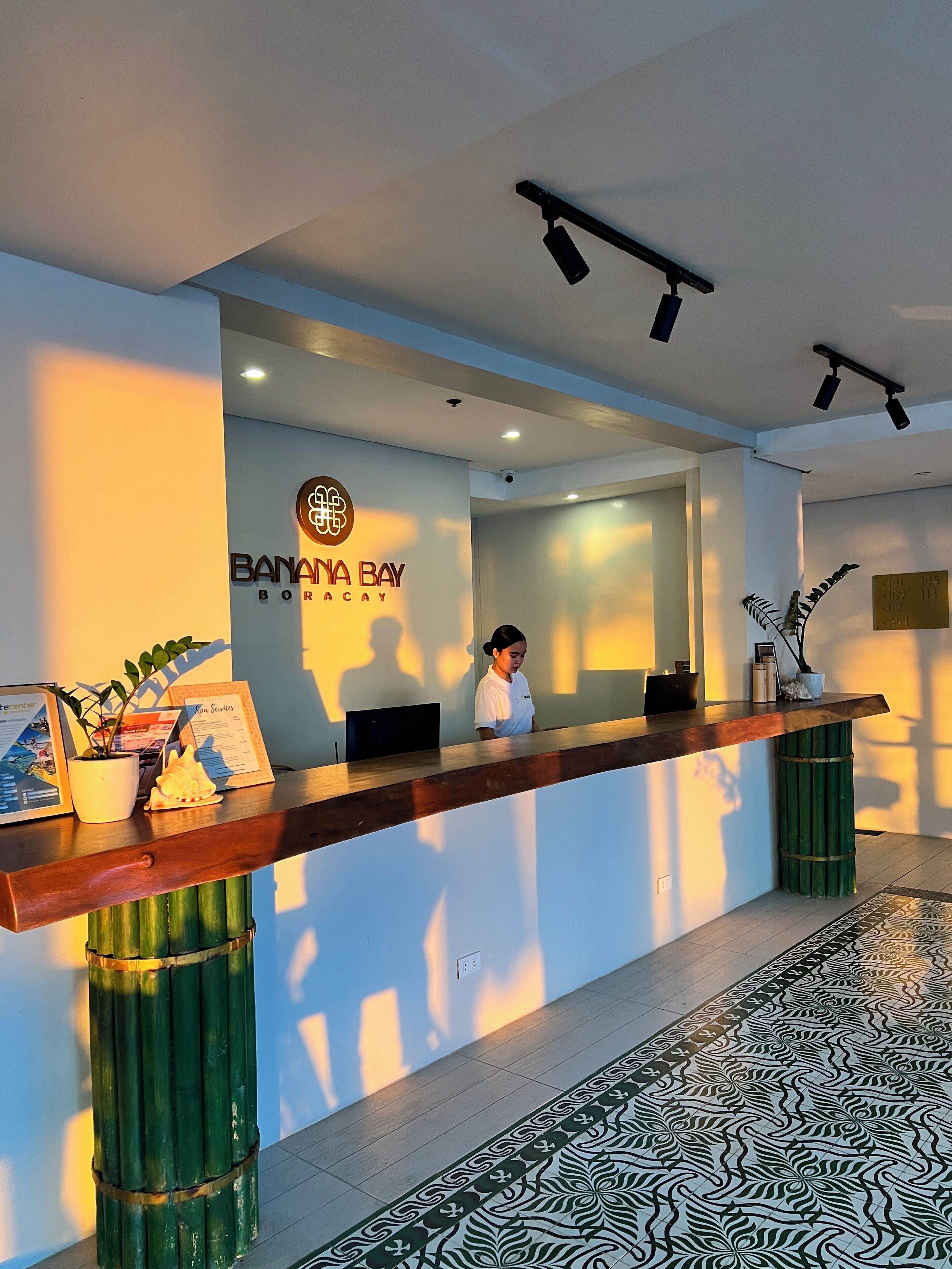 A reception desk with a sign for 'Banana Bay Boutique,' a potted plant, and a framed menu.