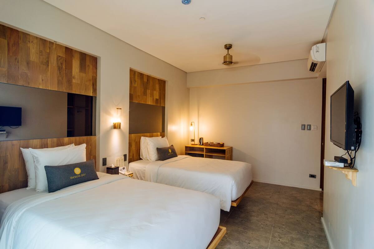 A hotel room with two beds, a TV, a ceiling fan, and a wooden accent wall.