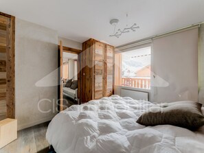 Ein Schlafzimmer mit einem Bett, einem Holzschrank und einem Fenster mit Blick auf eine verschneite Landschaft.