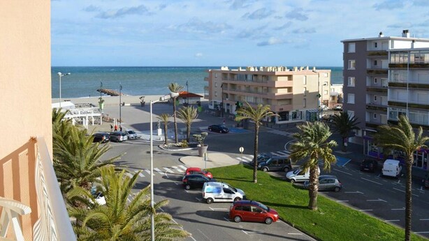 A coastal street with parked cars, a building with balconies, and a view of the sea. - Saint-Cyprien: 2-room apartment, sleeps 5, balcony, parking, near beach (Saint-Cyprien)