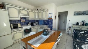 A compact kitchen with white cabinets, a microwave, an oven, and a coffee maker. There is a dining table with chairs and a black and white patterned cushion. - Saint-Cyprien: 2-room apartment, sleeps 5, balcony, parking, near beach (Saint-Cyprien)