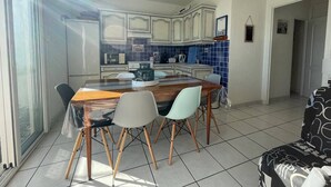 A dining area with a wooden table and chairs, a kitchen in the background, and a view through a glass door. - Saint-Cyprien: 2-room apartment, sleeps 5, balcony, parking, near beach (Saint-Cyprien)