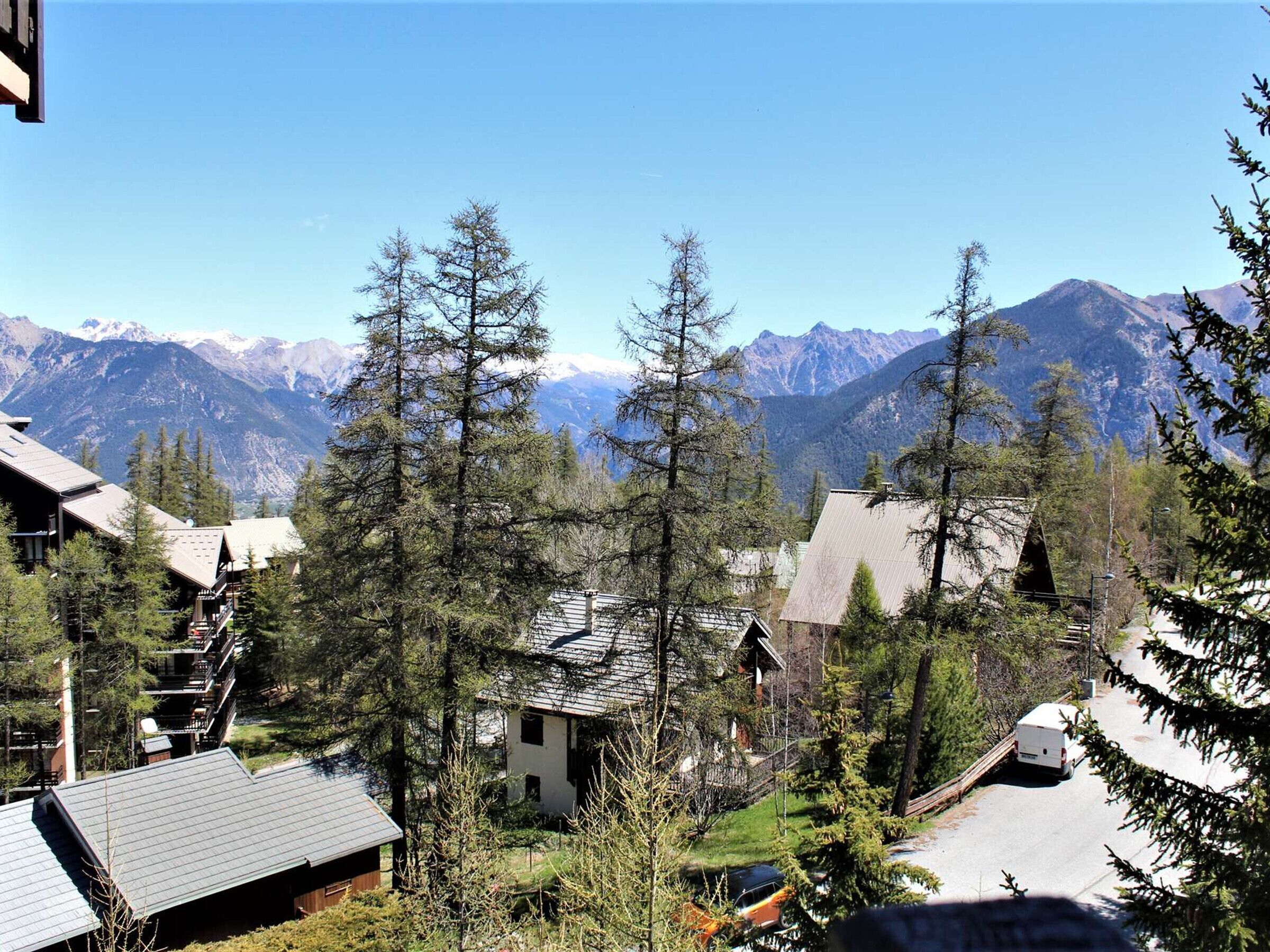 A mountain lodge with multiple buildings surrounded by tall pine trees and a view of snow-capped mountains.