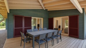 Eine Terrasse im Freien mit Tisch und Stühlen, ein Holzdeck und ein überdachter Bereich mit geneigter Decke.