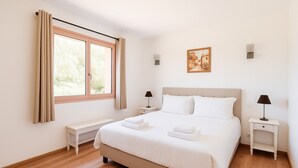 Ein Schlafzimmer mit einem großen Bett, einer Bank, Nachttischen, einem Fenster mit Vorhängen und einem Gemälde an der Wand.