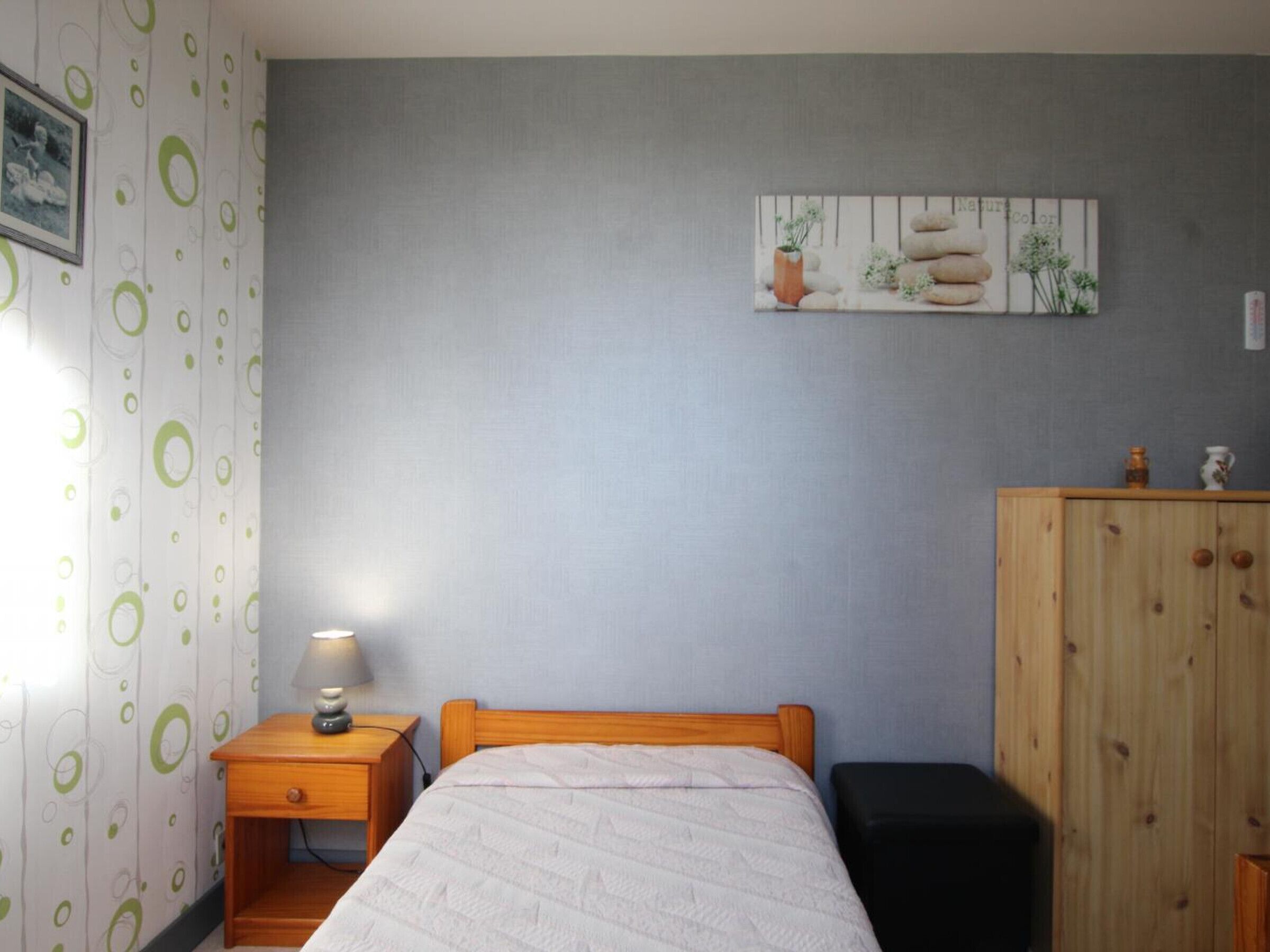 Une chambre à coucher avec un lit, une table de chevet avec une lampe, une armoire en bois et un mur orné d’un tableau.