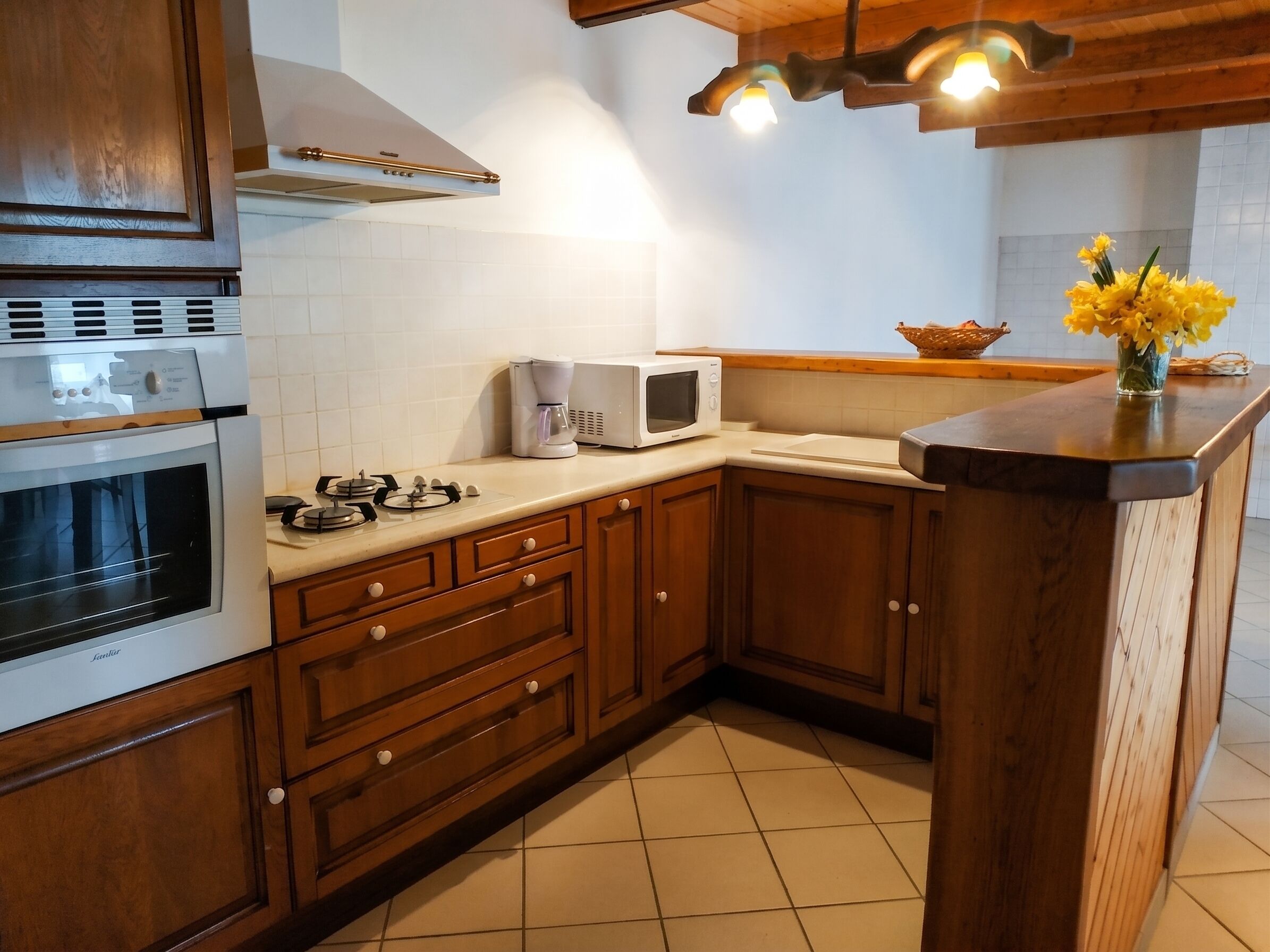 Een keuken met houten kastjes, een ingebouwde oven, een magnetron en een koffiezetapparaat op het aanrecht.