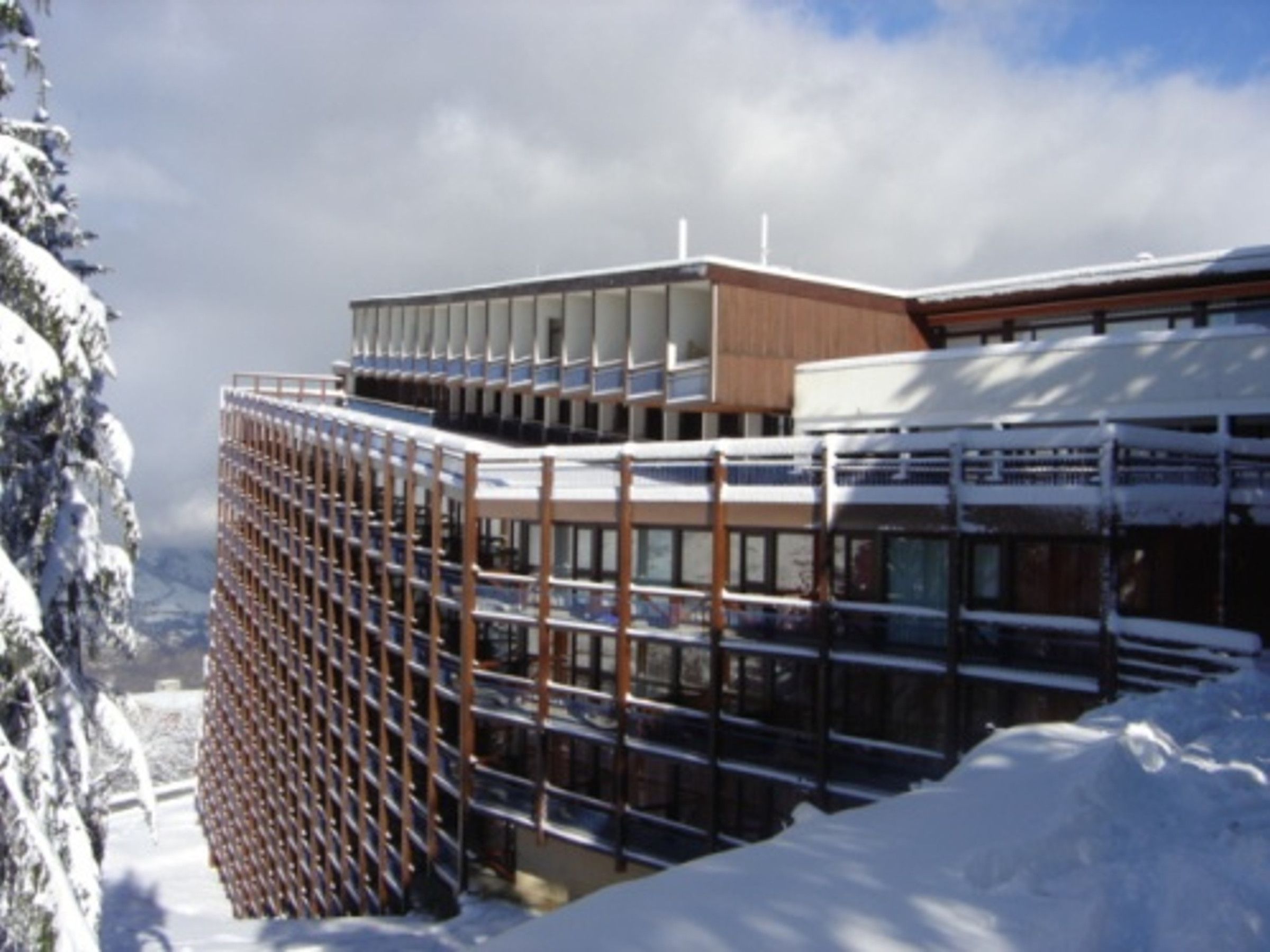 A modern building with a glass facade and wooden accents, surrounded by snow-covered trees.