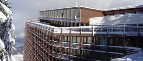 A modern building with a glass facade and wooden accents, surrounded by snow-covered trees.