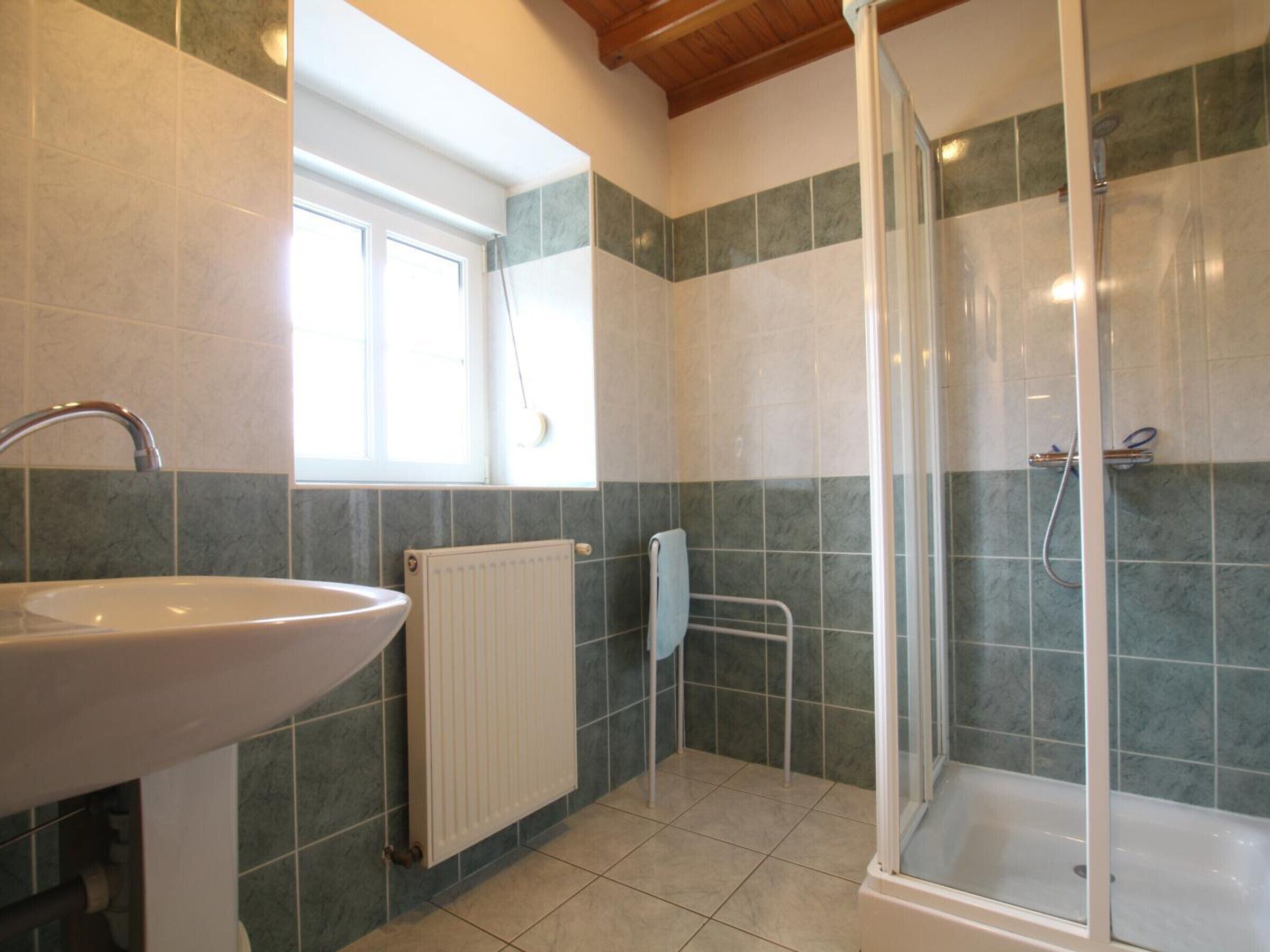 Een badkamer met een wastafel, een raam, een douche en een radiator.