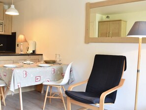 Uma área de refeições com uma mesa posta para dois, uma cadeira preta, um abajur e um espelho na parede.