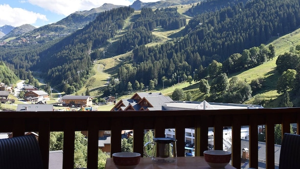 Vista de la montaña desde un balcón con baranda de madera, con vistas a un valle que incluye casas y un telesilla.