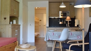 Un espacio habitable compacto con kitchenette, una zona de comedor con mesa y sillas, y un dormitorio con cama.