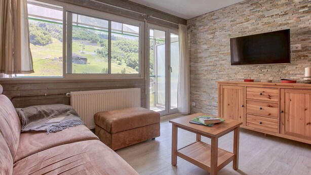 Un salon moderne doté d’une grande fenêtre, d’un canapé, d’une table en bois et d’un téléviseur fixé sur un mur en pierre.
