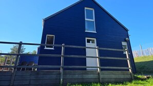 Ett tvåvåningshus målat i blått med en vit dörr och vita fönster, ett trästaket i förgrunden och en klarblå himmel.