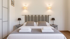 A neatly made double bed with a striped headboard, two bedside tables with lamps, and a framed picture on the wall. - Beautiful villa ' Les Figuiers' with pool between sea and mountain (Figari)