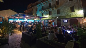 An outdoor seating area with wicker furniture, a covered section with blue lighting, and a stone building in the background. - Beautiful villa ' Les Figuiers' with pool between sea and mountain (Figari)