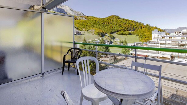 Un balcone con tavolo e sedie, vista su un paesaggio montuoso con edifici sullo sfondo.