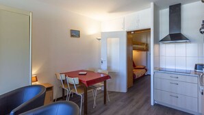 Una stanza compatta con tavolo, due sedie, angolo cottura e letto a castello.
