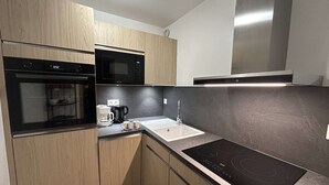 A modern kitchen with wooden cabinets, a black oven, a microwave, a coffee maker, and a sink. - 2-room apt for 4, 150m from slopes, Méribel (Méribel)