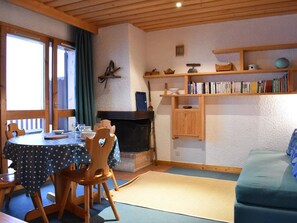 Een gezellige kamer met een eettafel, stoelen, een bank, een boekenkast en een open haard.