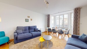 Ein modernes Wohnzimmer mit einem blauen Sofa, einem gelben Hocker und einem Esstisch mit Stühlen.