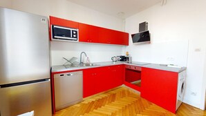 Eine kompakte Küche mit roten Schränken, einem Edelstahl-Kühlschrank, einer Mikrowelle, einem Geschirrspüler, einer Kaffeemaschine und einer Waschmaschine.