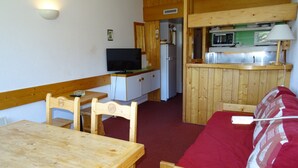 A compact room with a wooden dining table, a red sofa, a television, a kitchenette with a microwave, and a small refrigerator.