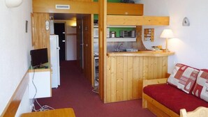 A compact room with a kitchenette, a bed, a desk, and a television.