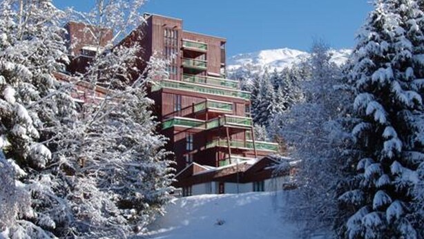 A multi-story hotel with balconies, surrounded by snow-covered trees and a clear sky.