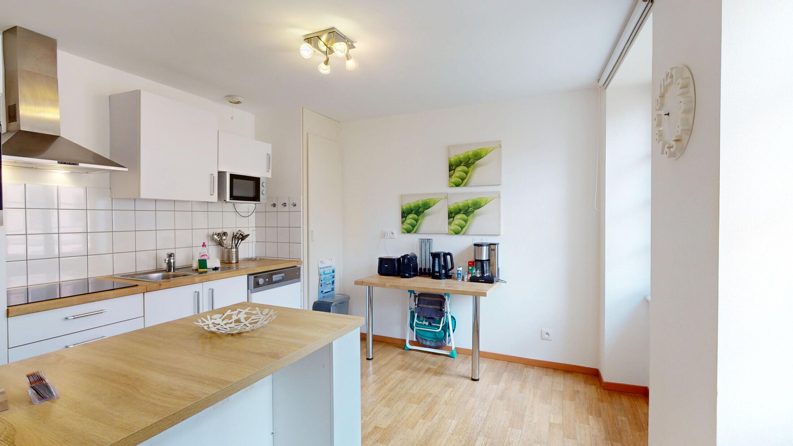 Une cuisine moderne avec des meubles blancs, un four à micro-ondes, une machine à café et une petite table avec un panier.