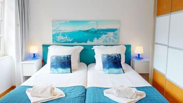 Un lit double avec du linge de lit blanc, deux oreillers ornés d’un motif représentant une scène de forêt, une tête de lit de couleur turquoise et un tableau représentant un paysage enneigé au-dessus du lit.