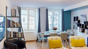 Un salon moderne avec un coin repas, de grandes fenêtres et une bibliothèque.