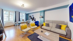 Una sala de estar moderna con un sofá, sillas, una mesa de centro y un comedor con una mesa dispuesta para dos personas.