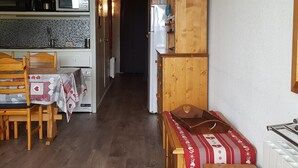 Una cocina compacta con armarios de madera, un microondas y un refrigerador. Un comedor con sillas se encuentra frente a la cocina.