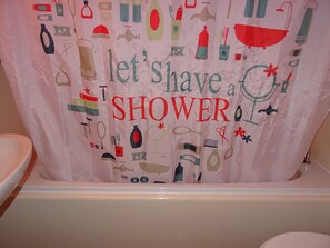 A bathroom with a shower curtain featuring various shower-related items and the text "let's shave a SHOWER".