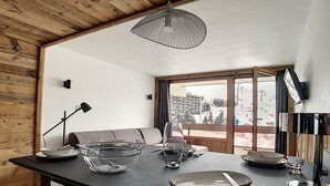 A modern kitchen with a wooden ceiling, a large window with a view of a snowy landscape, and a dining area with a sofa and table set.