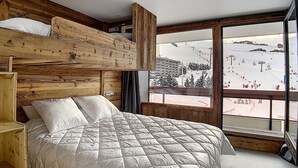 A bedroom with a bunk bed, a large bed, and a window with a ski slope view.