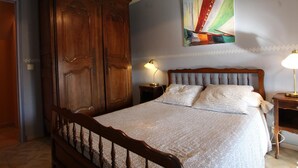 Een slaapkamer met een houten bedframe, een grote kledingkast, een schilderij aan de muur en twee bedlampen.