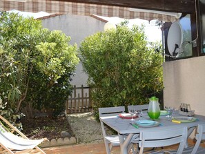 An outdoor patio area with a table set for dining, surrounded by lush greenery and a wooden fence.