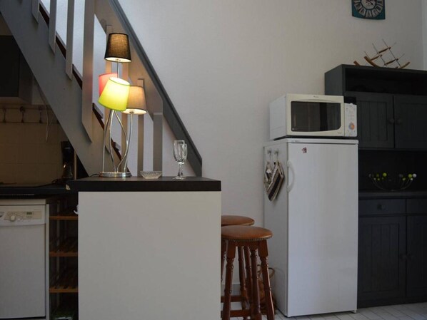 Eine kleine Küche mit einer Mikrowelle, einem Kühlschrank, einer Lampe und einem Weinglas auf der Arbeitsplatte.