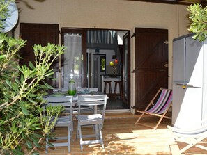 Eine Terrassenfläche mit Esstisch, einem Klappstuhl und einer kleinen Sitzecke mit gestreifter Sitzkissen.