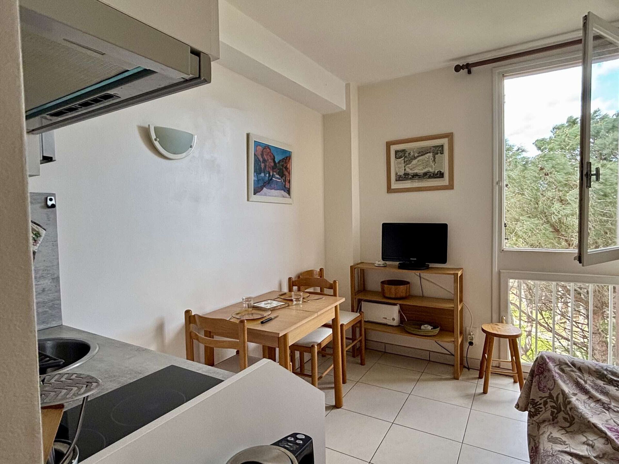 A compact living space with a dining area, a TV on a shelf, and a window with a view of trees.