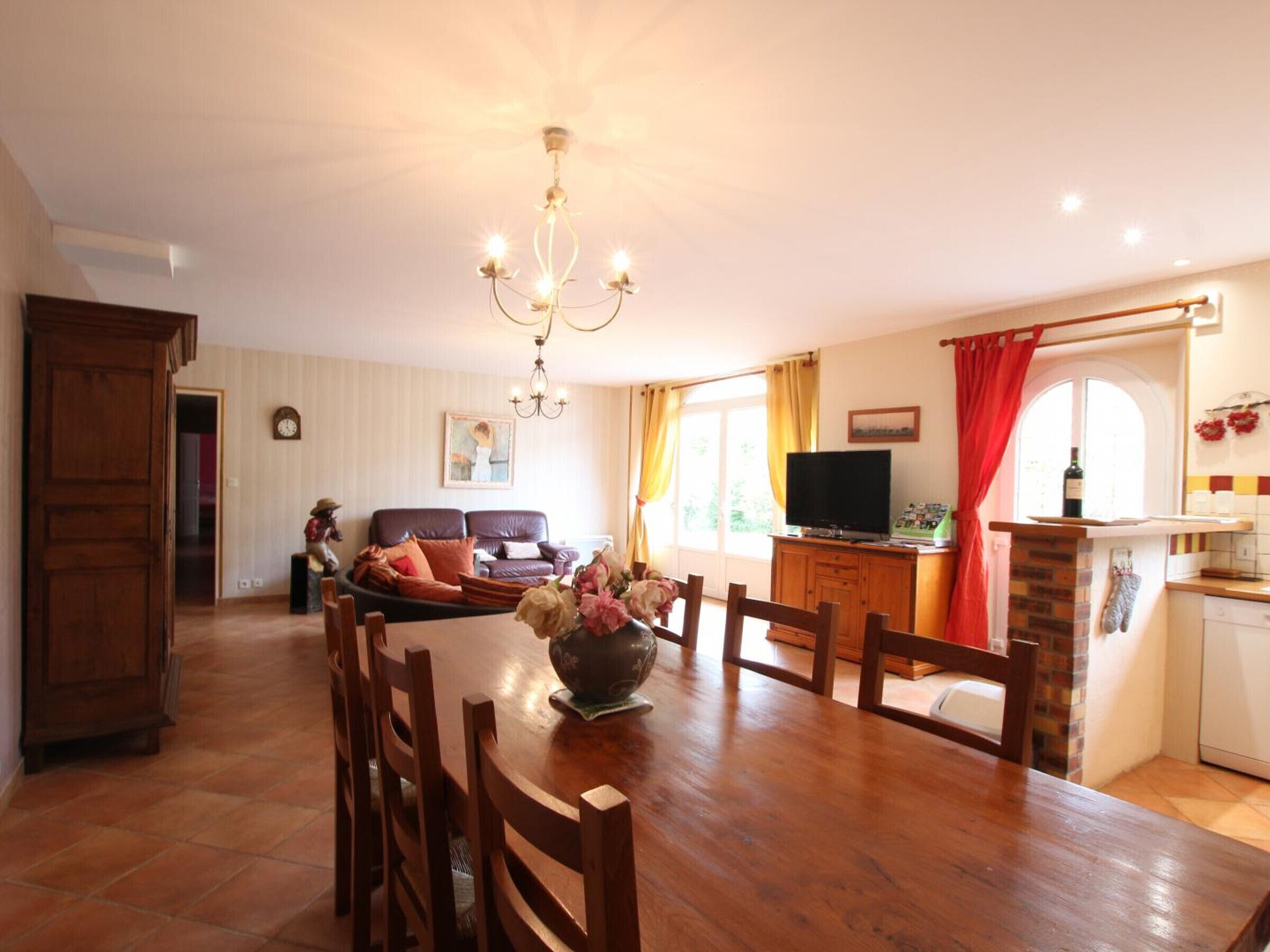 A spacious living room with a dining table, wooden chairs, a sofa, and a TV.