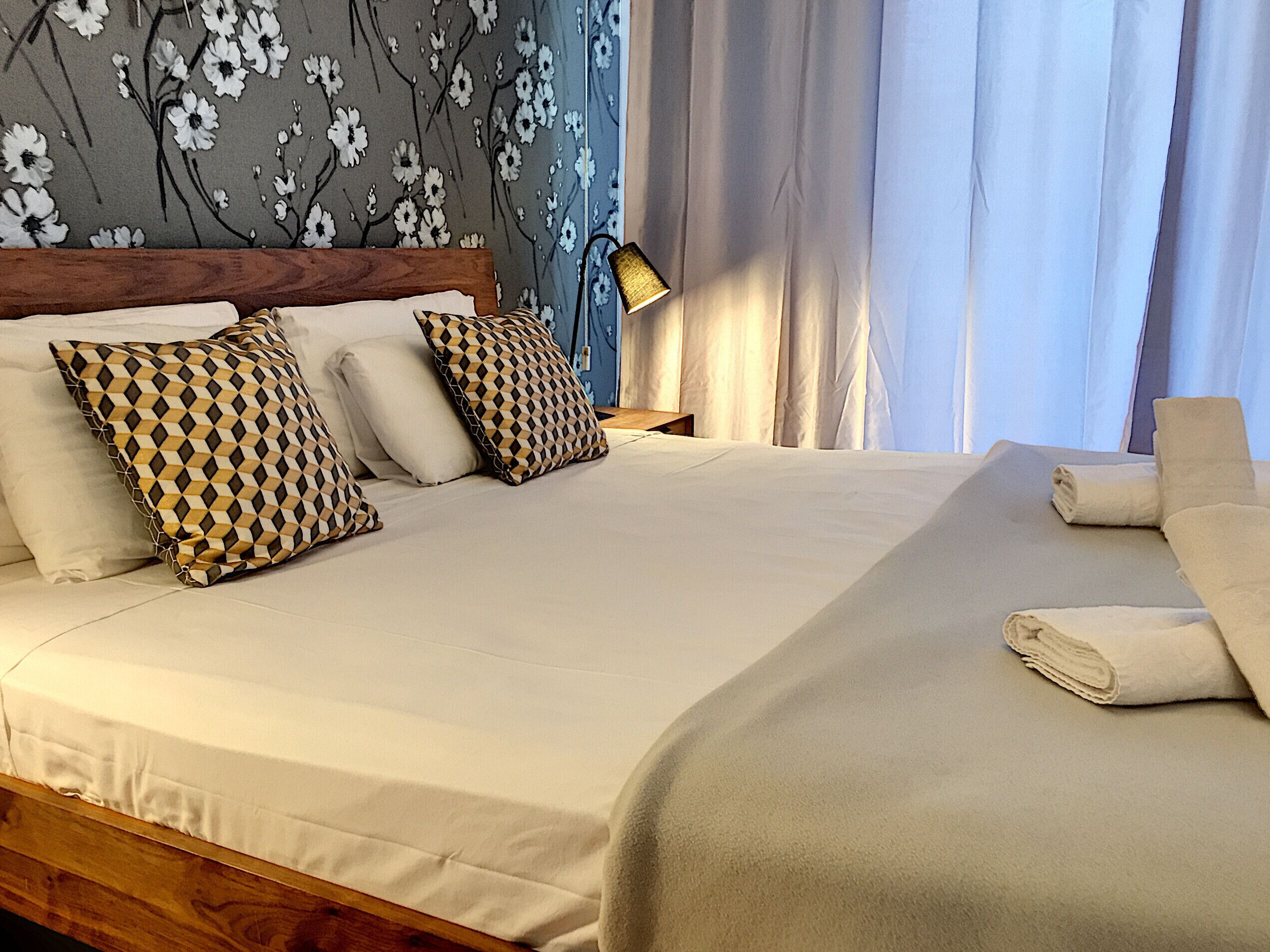 A neatly made bed with patterned pillows, a wooden headboard, and a nightstand with a lamp.