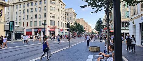 A busy urban street with tram tracks, pedestrians, and various commercial buildings including a hotel.