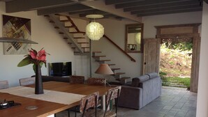 A modern kitchen with a wooden island, a dining area with chairs, a sofa, and a staircase leading to a balcony.