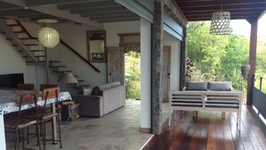 A spacious living area with a wooden floor, a sofa, a dining table with chairs, and a staircase.