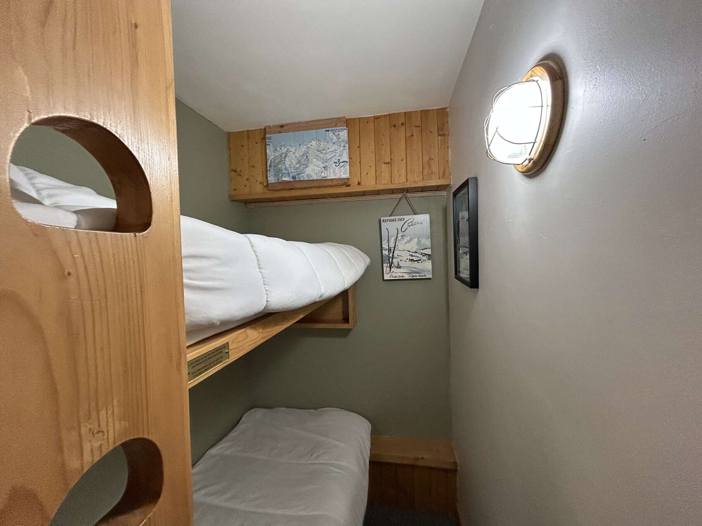 A compact room with bunk beds, a small shelf with a framed picture, and a wall-mounted light fixture.