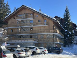 A multi-story wooden building with balconies and a stone facade, surrounded by snow and trees.